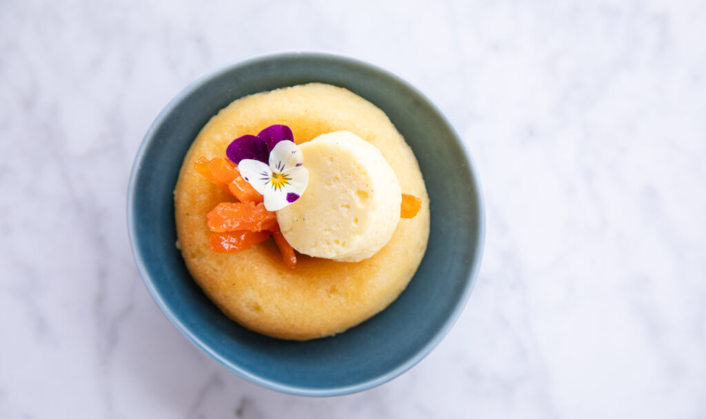 overhead of yellow cake in blue bowl with edible flowers and apricot