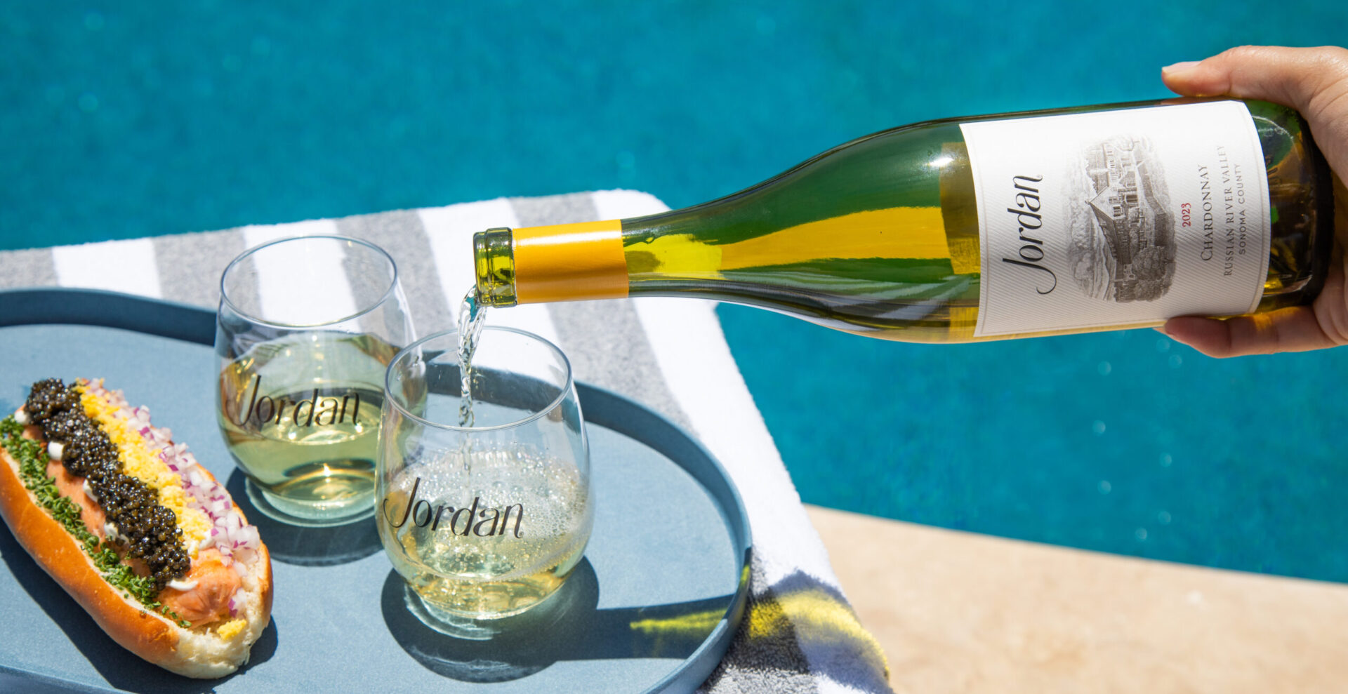 chardonnay bottle pouring into stemless wine glasses by the pool