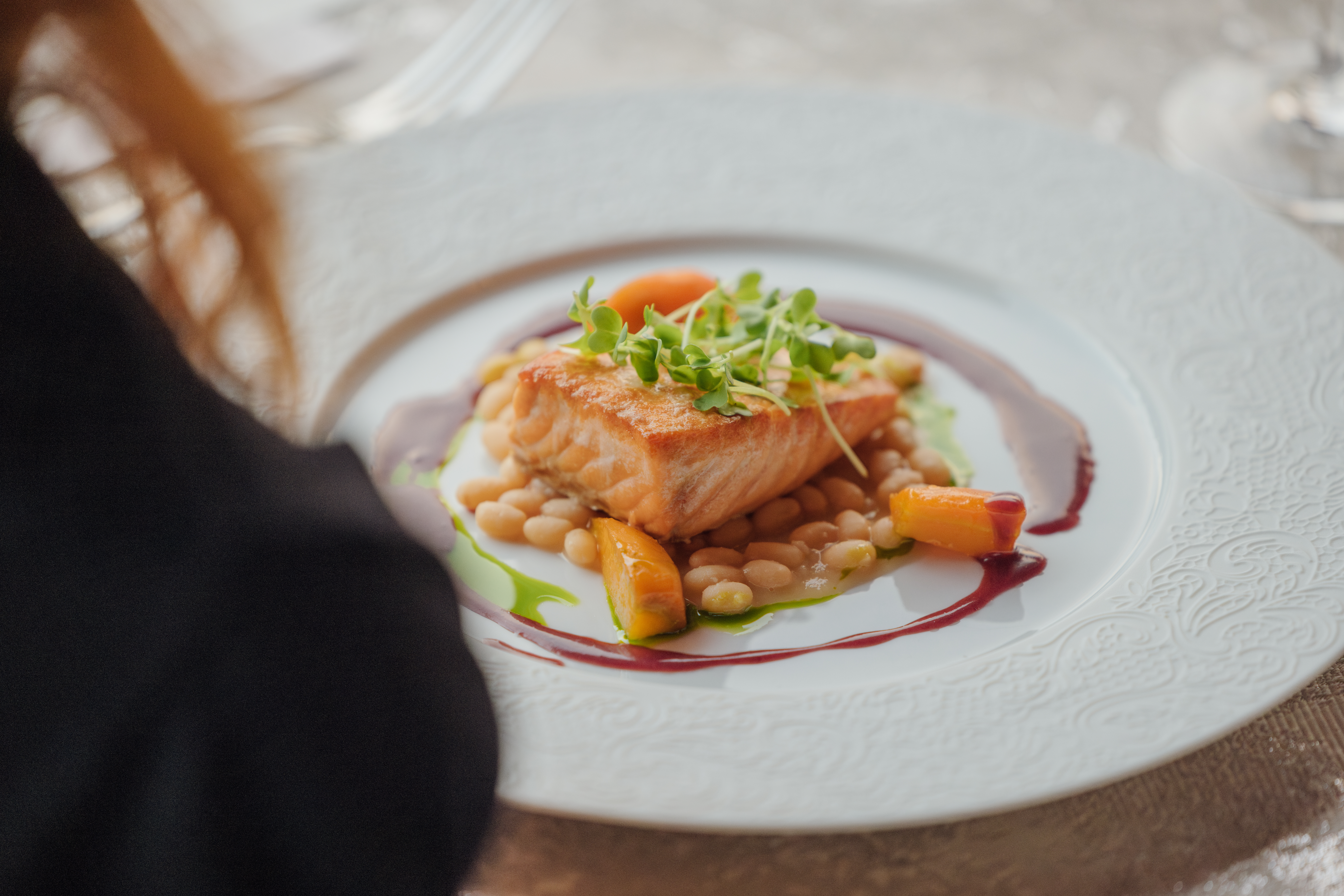 over the shoulder of person's dinner plate of salmon and vegetables
